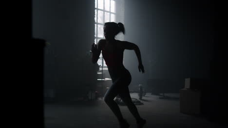 active sportswoman jogging in dark loft building. strong woman running in gym