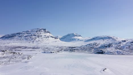 aerial view of group of people on snowmobiles going over frozen lake in snowy mountain landscape