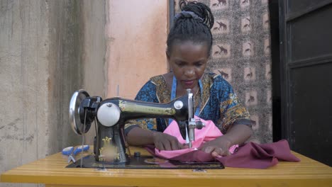 Vorderansicht-Einer-Afrikanerin,-Die-Vor-Ihrem-Kleinen-Haus-Auf-Einer-Schneidermaschine-In-Afrika-Stoffe-Näht