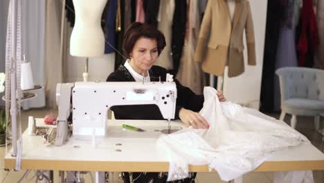 portrait of female tailor working on sewing machine. caucasian woman using a sewing machine at studio or in workshop. skillful expert tailor works on sew machine with a white pattern, sparkling fabric