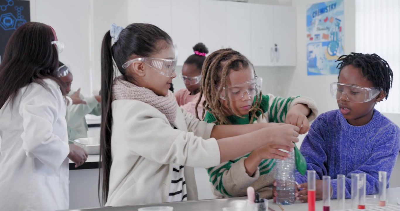 Students in goggles fitting green balloon on clear bottle, teacher in lab coat guiding for science