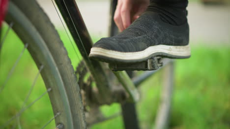 close-up of someone wearing grey sneakers tapping and rotating bicycle pedal in grassy field, places his foot on the pedal, adjust the sneaker with blurred background a greenery