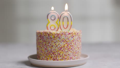 studio shot birthday cake covered with decorations and candle celebrating eightieth birthday being blown out