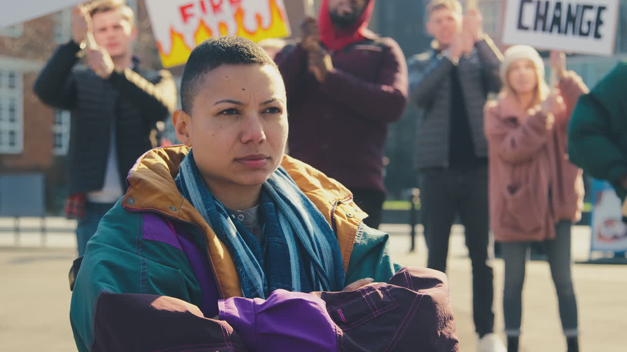 시위에 대한 표지판을 들고 행진자들에 둘러싸인 체어에 앉은 여성 시위자