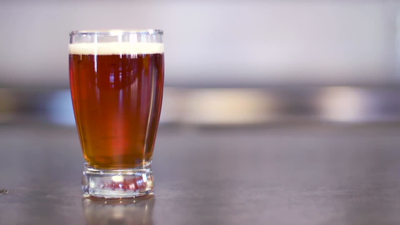 Close up static shot of a brown amber glass of beer with a small foam head on a silver table