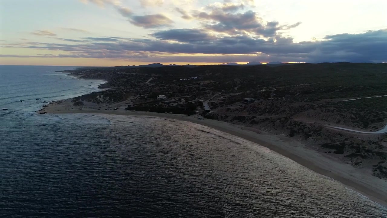 Il drone si allontana dall'alto sopra l'acqua a Nine Palms, con vista sul paesaggio desertico verde nella luce del crepuscolo, tornando indietro sopra l'oceano per rivelare l'intera spiaggia, la punta, le onde sottostanti e la c