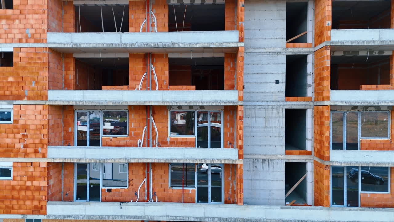 Close-up da fachada de um edifício de apartamentos em construção com paredes de tijolo. Vista exterior de um edifício residencial de vários andares mostrando tijolos vermelhos e varandas de concreto sem grades.