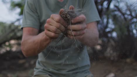 Caucasian-male-survivalist-preparing-tinder-bundle-to-make-fire-at-camp-in-wilderness