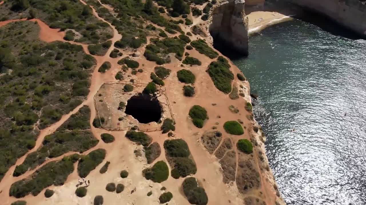 Drone view of rugged coastal cliffs with natural cave formations and clear water near sandy beach under bright sunlight near Douro River Valley in southern Portugal