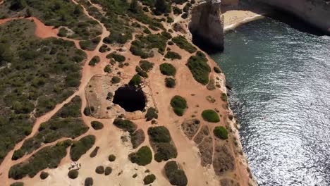 drone view of rugged coastal cliffs with natural cave formations and clear water near sandy beach under bright sunlight near douro river valley in southern portugal
