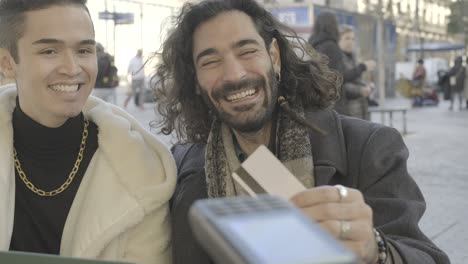 two men laughing while one is paying with a card