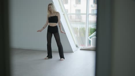 fit girl in black clothes performing contemporary. female dancer shows flowing motions, body and hands waves at white room. modern ballet dance choreography. young woman is moving smoothly