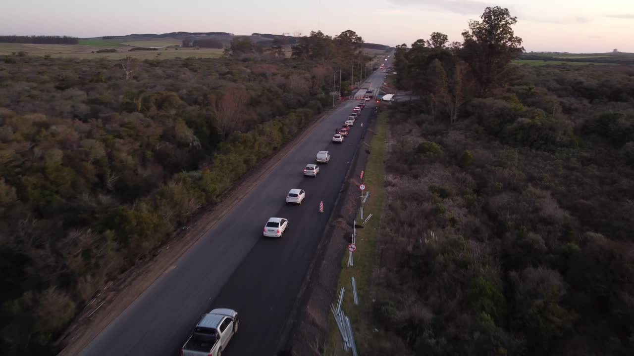 Fila de autos haciendo cola en una carretera rural rectilínea de Uruguay.