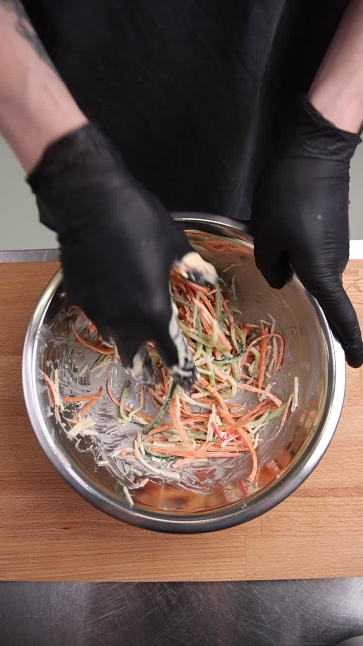 Mains de chef mélangeant une salade fraîche dans un bol en métal