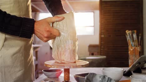 alfarero quitando la cubierta de plástico de la arcilla de moldeo en el taller de cerámica