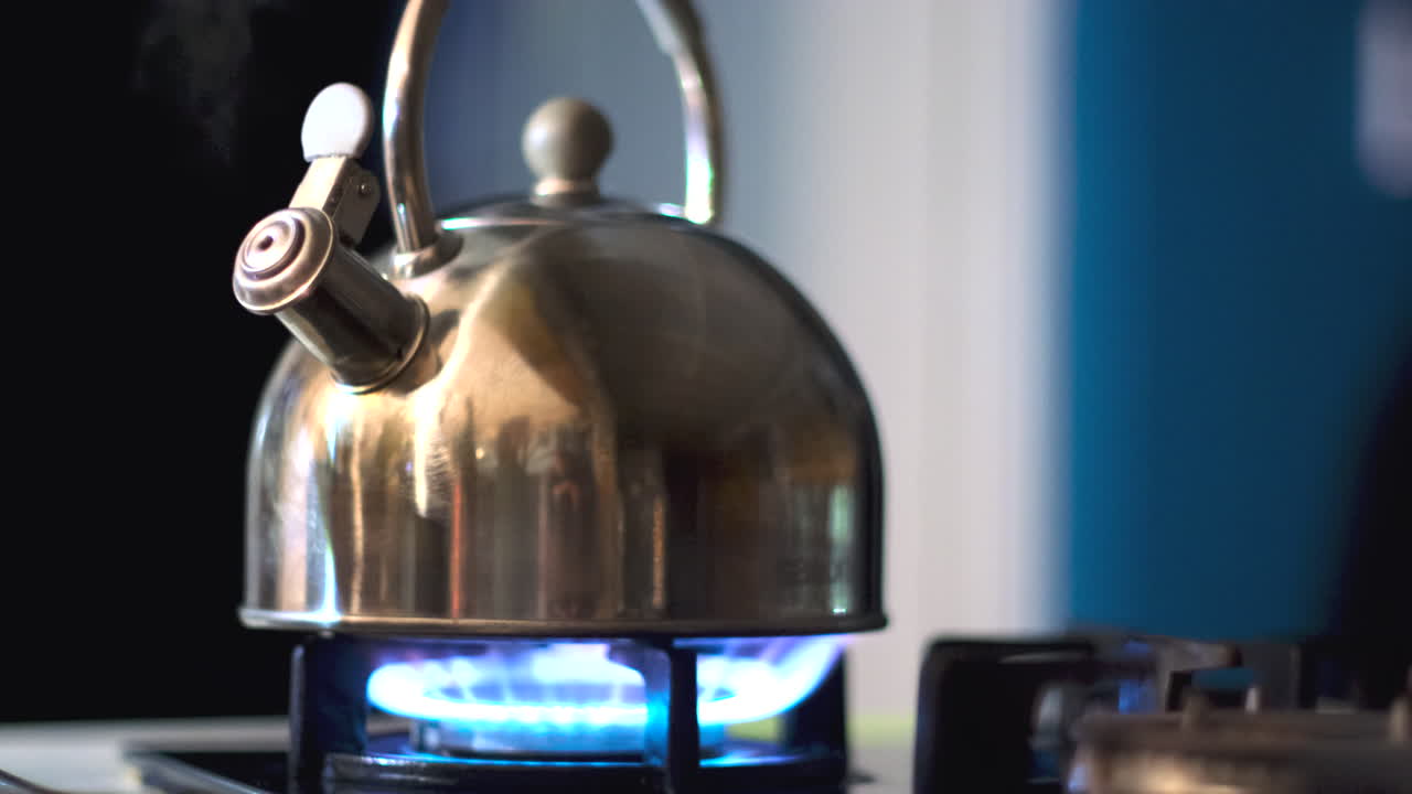Blue gas flame of hob heats and boils water of whistling stainless steel kettle