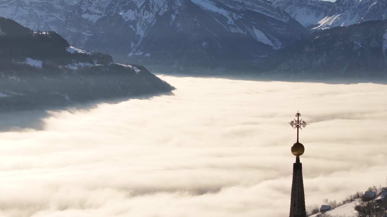 Stunning aerial view of Walensee, Switzerland with breathtaking sea of clouds covering valley, snowy Swiss alps, golden sunrise and mystical fog winter landscape.