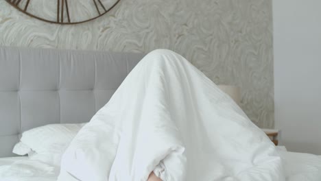 young happy and cheerful woman playing hide and seek under her quilt