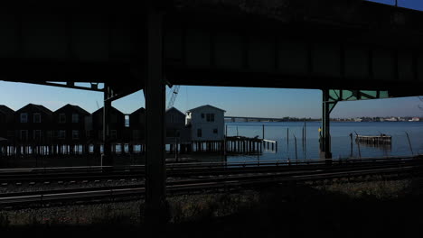 A-drone-shot-in-front-of-elevated-train-tracks-near-a-bay-in-Queens,-NY