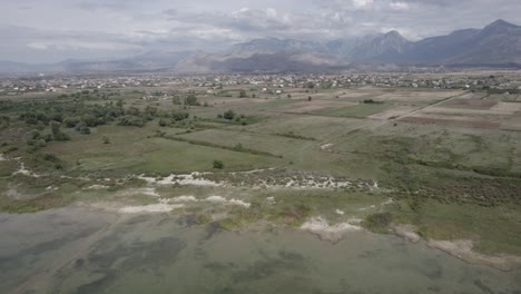 Video-Mit-Einer-Drohne-über-Dem-Skadar-See-In-Albanien,-Aus-Einem-Anschaulichen-Flugzeug-Mit-Rückwärtsgang,-Das-Das-Grude-Fushe-Dorf-Am-Horizont-Mit-Den-Bergen-Verlässt