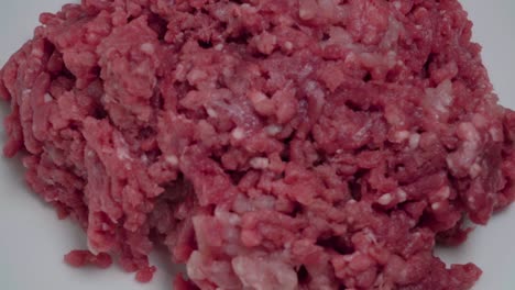 overhead, rotating raw ground beef meat on white plate, closeup