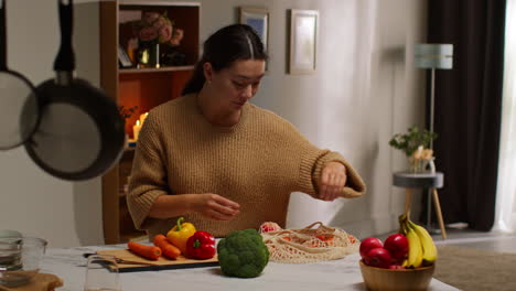 mujer volviendo a casa de las compras de comida desempaquetando una bolsa de verduras frescas en el mostrador en la cocina