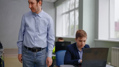teacher assisting students with laptops in a classroom