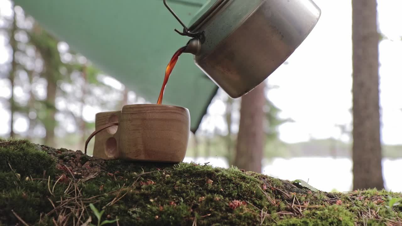 Coffee poured to a wooden cup from a steel coffee pot in a camping setup in Repovesi national park in Finland, stationary shot