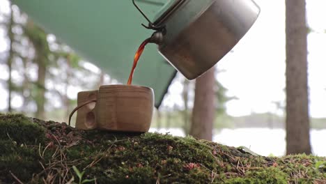 coffee poured to a wooden cup from a steel coffee pot in a camping setup in repovesi national park in finland, stationary shot