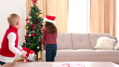hermanos lindos poniendo regalos bajo el árbol de navidad