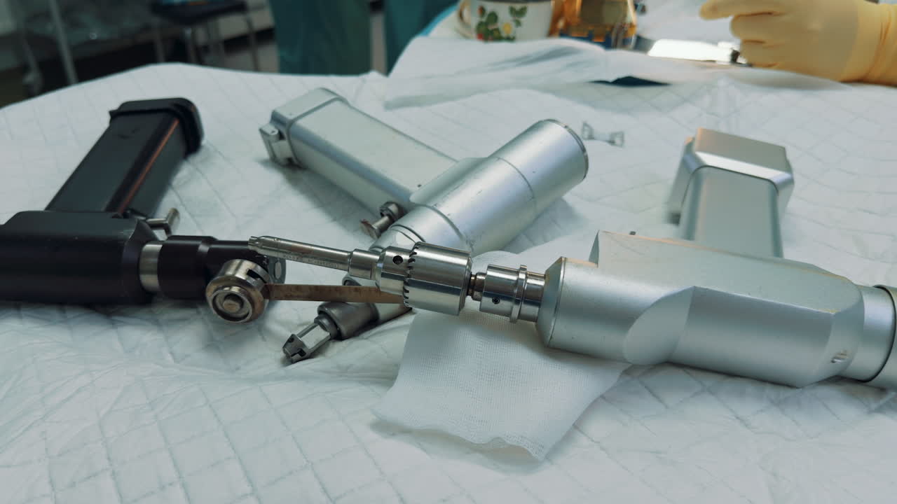 Close-up of power tools and a drill bit used for orthopedic surgery. The instruments are laid out on a sterile white cloth, ready for the medical procedure