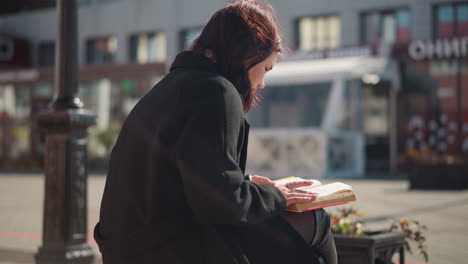 back view of a lady deeply focused on reading her book outdoors as her hair gently sways in the breeze, sunlight creates a silhouette effect