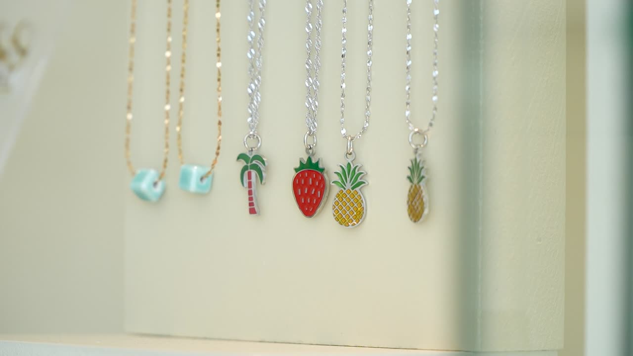 A charming collection of necklaces featuring playful designs like pineapples and palm trees is showcased in a bright jewelry store. The vibrant colors attract attention