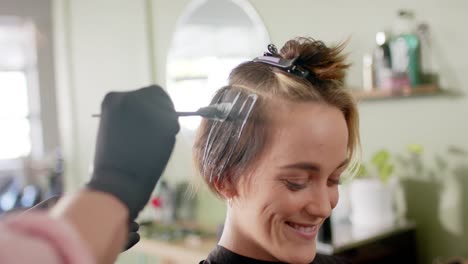 mano de un peluquero caucásico tiñendo el cabello de una cliente feliz en el salón, en cámara lenta