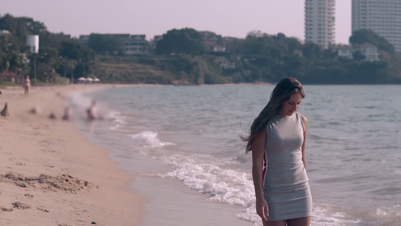 회색 드레스를 입은 아름다운 긴 머리카락의 갈색 여성이 맨발로  ⁇ 고 있습니다.