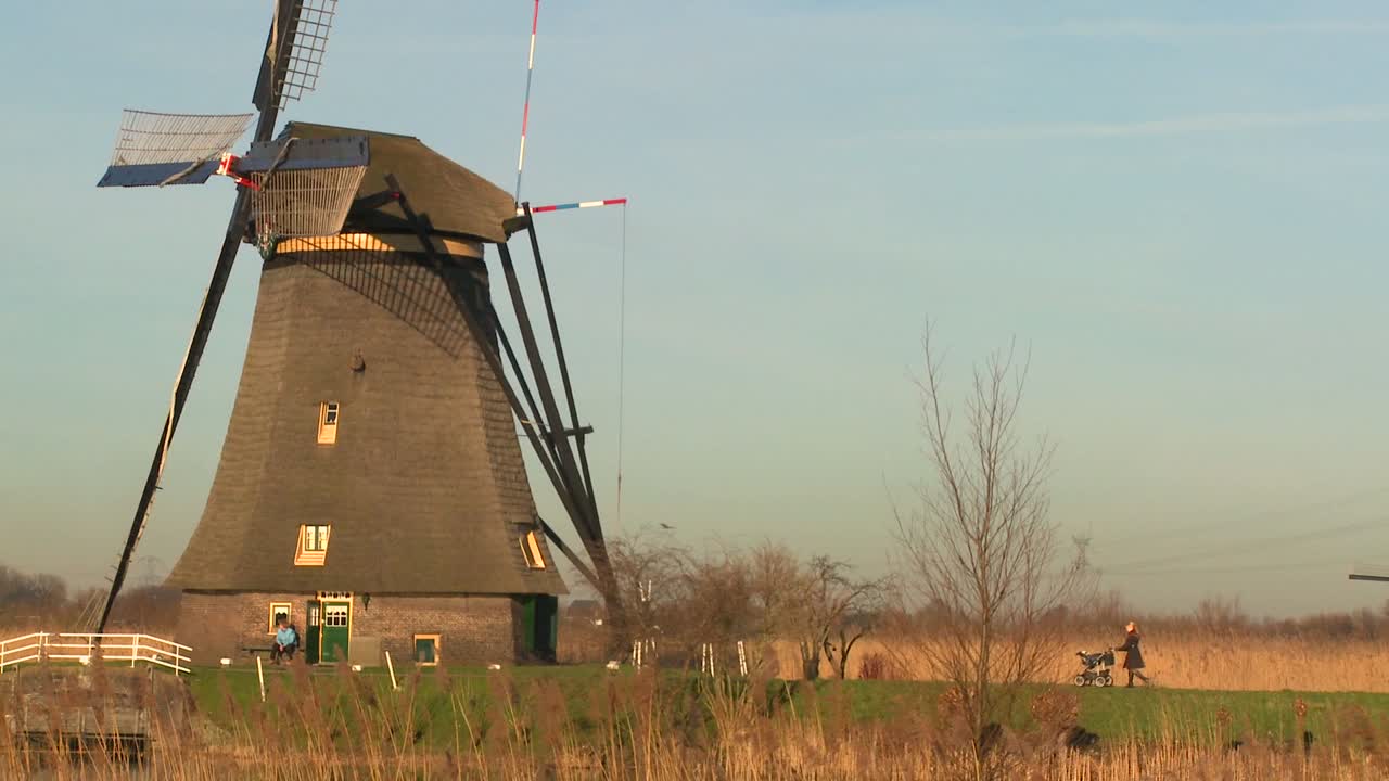 женщина толкает детскую коляску по тропинке возле ветряной мельницы в голландии