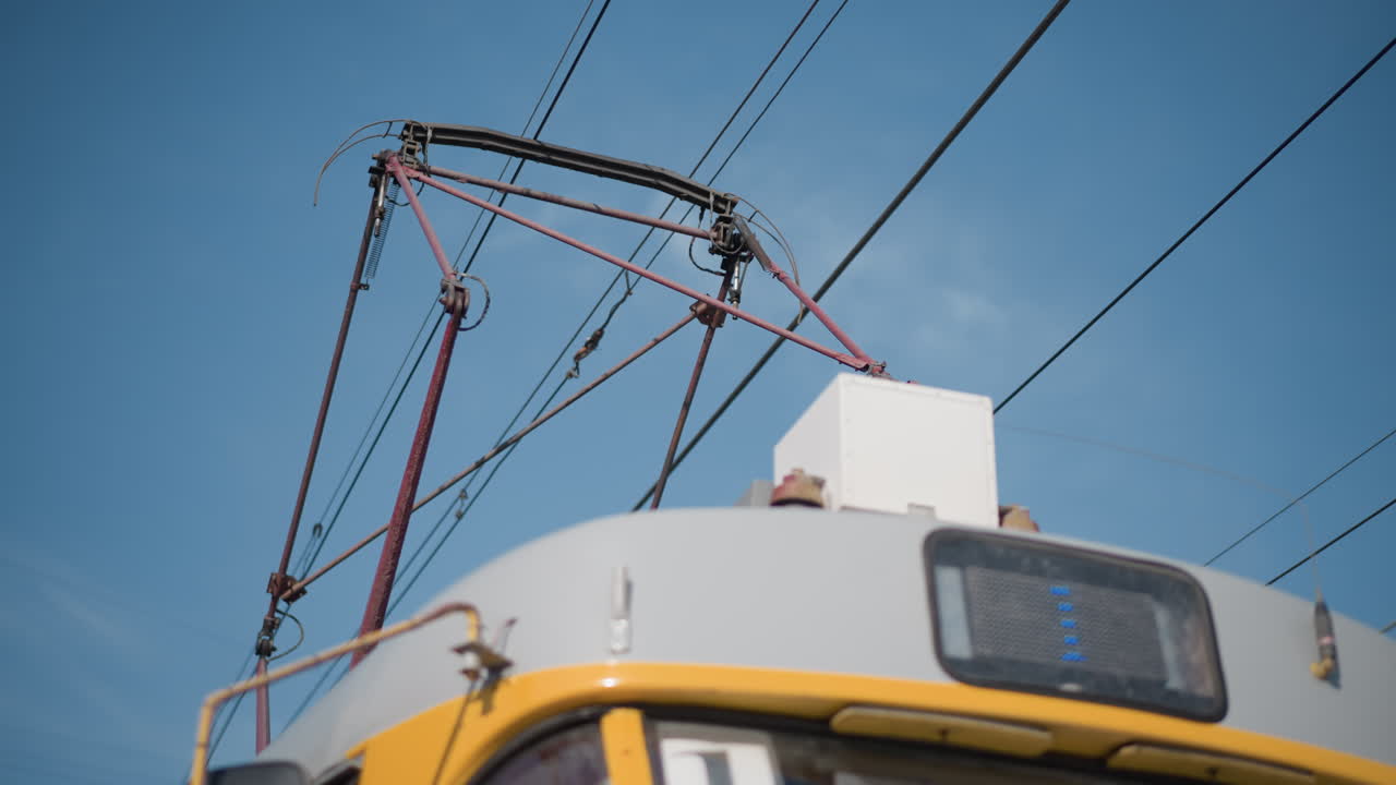 Sky view electric transit wires under clear blue sky, sun shining behind power lines, tram pantograph frame visible, minimal urban scene, perspective lines crossing, bright winter daylight, city mood