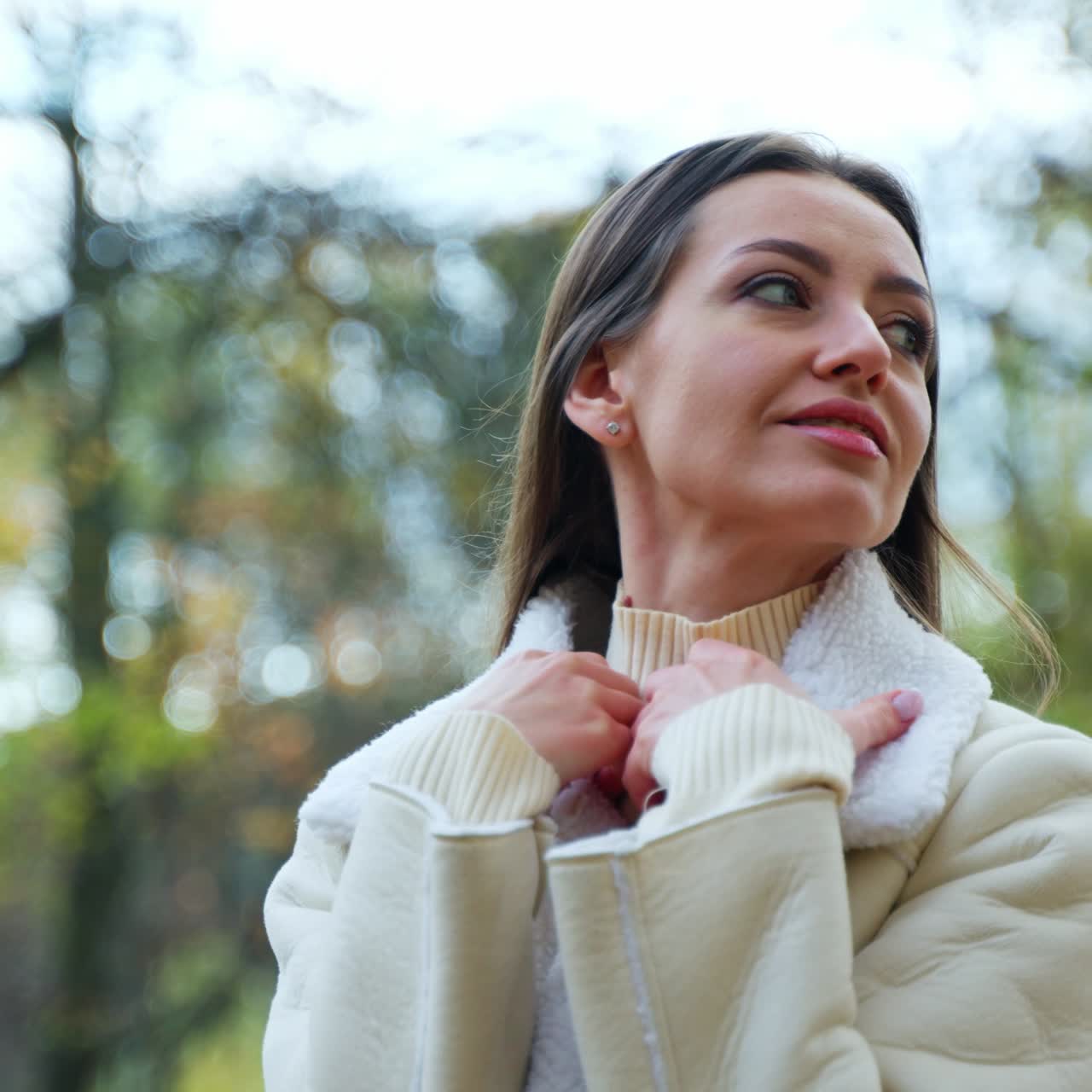 Beautiful brunette wrapping herself up in a jacket sitting outdoors. Lady spending free time in the autumn park. Close up