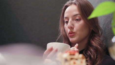 lady gently blows steam off latte while gazing pensively in calm atmosphere, lost in thought with relaxed expression. soft background blur and warm lighting create tranquil moment