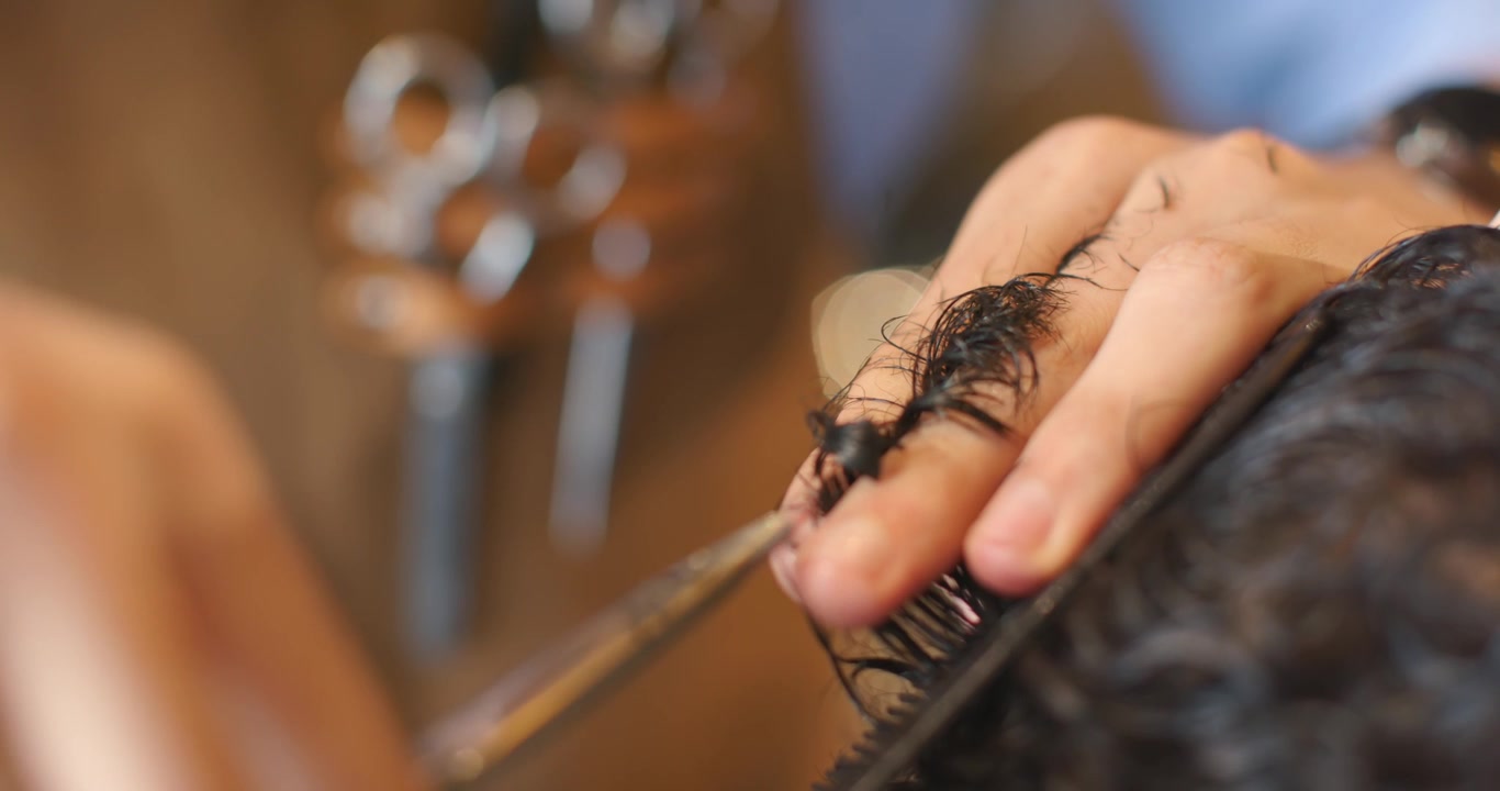 Barbiere africano che prende i capelli tra le dita, tagliando ricci scuri e bagnati con le forbici in un negozio, dando forma all'acconciatura.