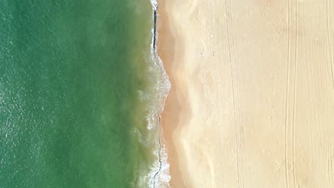 elevated view of green ocean surf crashing on golden beach