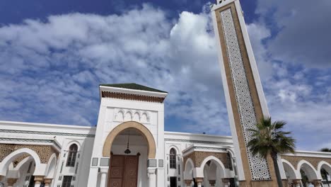wide angle view of the masjid lalla abosh mosque in tangier, morocco, featuring its white facade, arches and minaret under a cloudy blue sky
