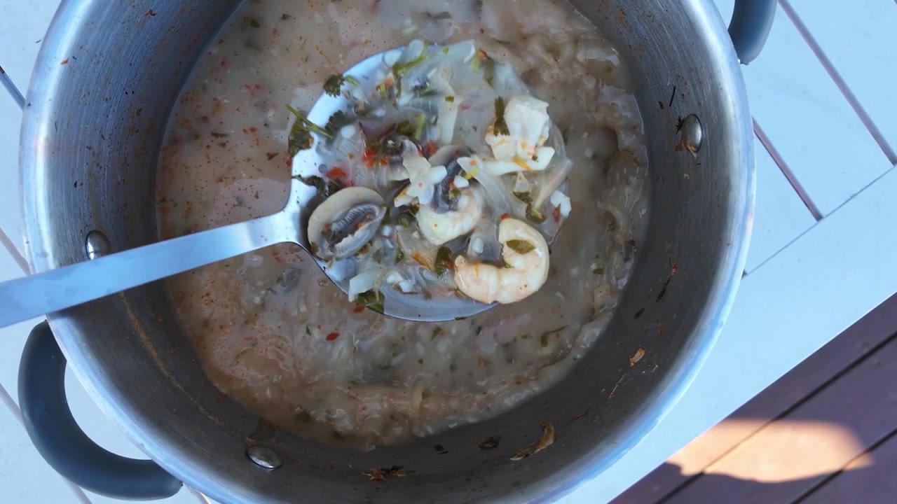 Ovenfra-bilde av en metalløse som rører krydret sjømatssuppe med sopp i en gryte