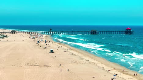 Drone-flying-over-Huntington-Beach-looking-at-the-Pier-and-some-large-waves-breaking-on-the-shore