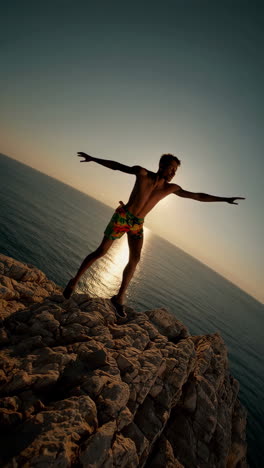 young man on cliff overlooking ocean at sunset