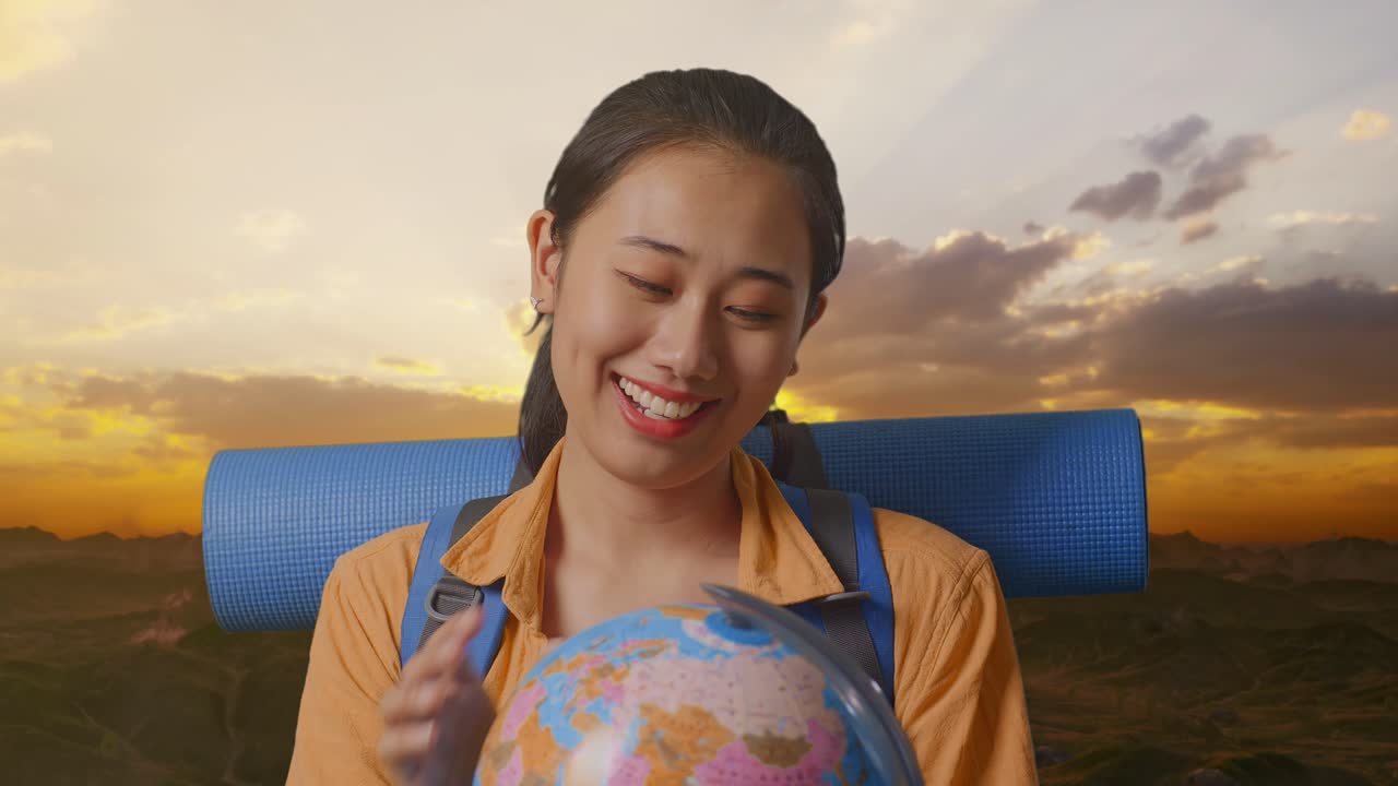 close up de una excursionista asiática con mochila de montañismo sosteniendo el globo mundial en sus manos y sonriendo mientras está de pie en la cima de la montaña durante la hora de la puesta del sol