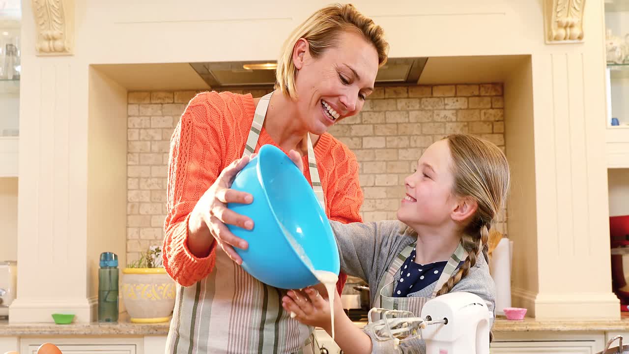 Smiling mother and daughter wearing apron pouring mixture for baking 4K 4k