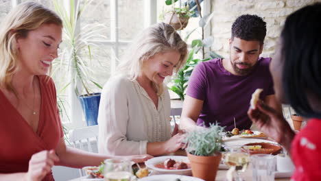 multi-ethnic group of young adult friends eating lunch together at a restaurant, side view