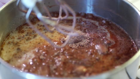 A-chef-pouring-milk-into-a-mixing-bowl-full-of-cocal-powder-and-flour-and-using-an-electric-mixer-to-make-chocolate-cake-batter-while-baking-in-the-kitchen