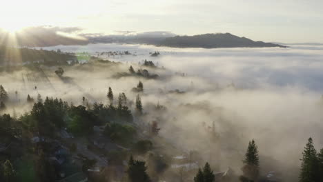 Dreamy-aerial-view-of-city-immersed-in-fog-at-sunrise-with-sun-rays-present